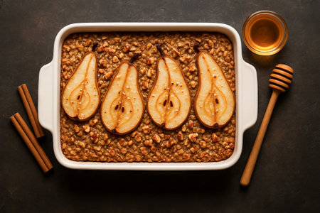 Pear oatmeal delight dessert in white ceramic dish with honey and cinnamon sticks on dark background. concept of healthy breakfast, homemade dessert, nutritious meal.の写真素材