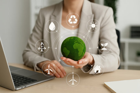 Young Caucasian woman holding a green globe surrounded by environmental symbols in a modern office. Concept of sustainability innovation and climate awarenessのeditorial素材