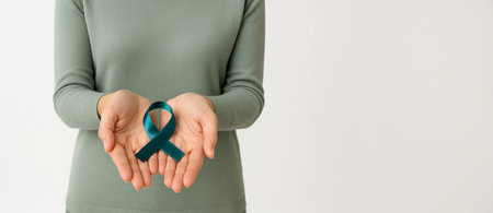 Woman holding teal awareness ribbon in hands on white background with copy space. Concept of ovarian...