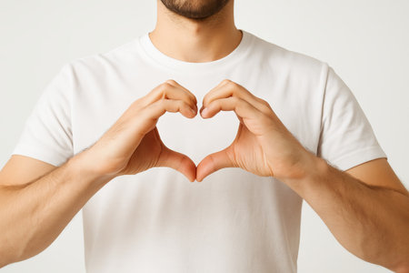 Close-up of heart gesture by young adult in white t-shirt. concept of love, romance, human connection, simple expression, positive emotions, kindness and affection, white background.の写真素材