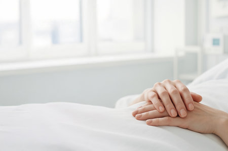 Folded hands of patient resting on white hospital bed in bright cozy room with large window. Concept of hospital recovery, peaceful medical care, patient support, calm healing environment, copy space.の写真素材