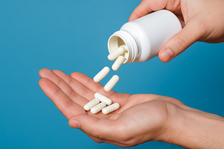 White pills falling from bottle into hand against blue background. concept of medicine, healthcare, prescription, pharmaceutical, medication, treatment, healthcare product.の写真素材