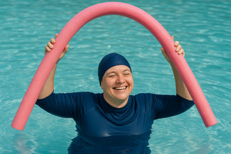 Smiling woman enjoying pool exercise with pink foam noodle on a sunny day. concept of water workout,...