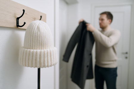 Man in winter coat adjusting garment in sleek modern entryway with cozy wool hat on hook, concept of fashion, home interior, winter style.の写真素材