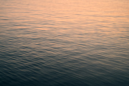 Tranquil ocean waves at sunset with gentle ripples on water surface depicting a serene and peaceful seascape illustration, concept of calmness, nature, relaxation.の写真素材