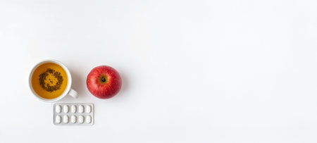 Tea with herbal infusion accompanied by red apple and pills on white background. concept of health, natural remedies, daily wellness, banner, copy space.の写真素材