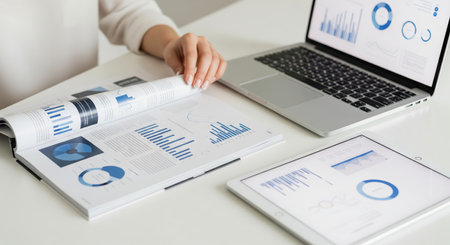 Businesswoman analyzing data charts and graphs in a professional office with a laptop and tablet....