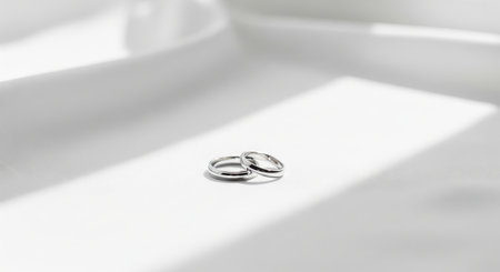 Trendy white color 2026 year. Two silver wedding rings on a white fabric surface with subtle shadow accents. Romantic marriage symbol for wedding invitation or anniversary celebration..の写真素材