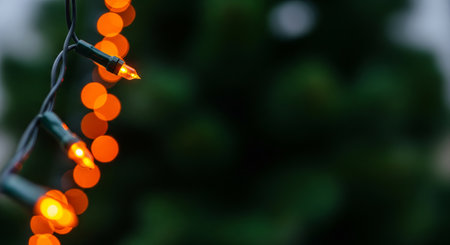 String of warm orange Christmas lights with bokeh effect against a dark green background. Festive holiday decoration for Christmas and New Year celebration. copy space.の写真素材