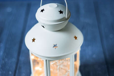White vintage Lantern with burning candles, pine cones on wooden table and glitter lights...