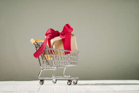 Christmas creative minimal composition. Shopping cart and Xmas gift, red satin bow on black background. Christmas, New Year, winter concept, copy space.の写真素材