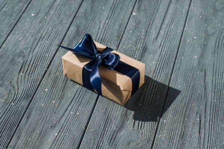 Brown gift box and red ribbon with tag on wood background with space.