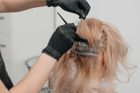 Hairdresser hands bleaching strands of blonde woman hair in beauty salon. Closeup.の写真素材