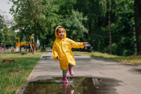 Girl in a yellow dress with an umbrella joyful spring runs through the puddles on a rainy dayの写真素材