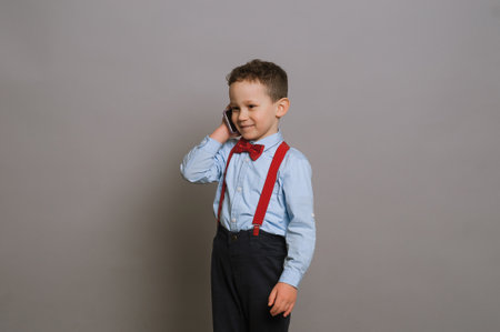 a smart boy 5-7 years old in a business image on a gray background holds a pig piggy bank in his handsの写真素材