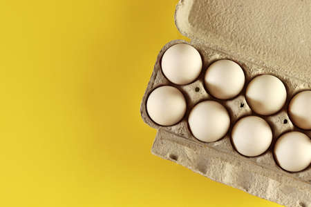 White chicken eggs in an open cardboard box with eggs isolated on yellow. Fresh chicken eggs background. Top view with copy space. Eggs in a boxの写真素材
