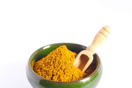 Heap of curry powder in a ceramic bowl with wooden spoon isolated on white background. Spices and herbs. Close up, top view. Free space for text.の写真素材