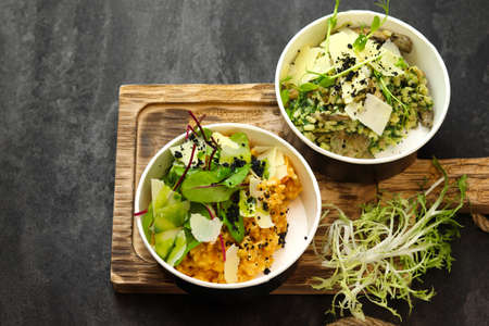 Risotto with tomatoes, greens, mushrooms and parmesan in bowls on wood board on black background. Restaurant dish delivery. top view. Free space for text. Healthy food concept.の写真素材