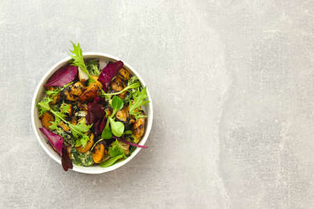 Salad with mussels, arugula and greens in a round takeaway paper container on gray background. Healthy food delivery concept. Banner. top view.の写真素材