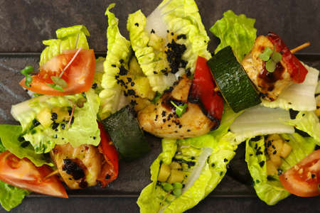 Grilled vegetable and chicken skewers with bell peppers, zucchini, tomatoes and lettuce on black background, top view, restaurant dish.の写真素材