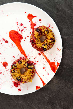 Vegan donuts topped with healthy red glaze with blueberry and flakes on white plate isolated on...