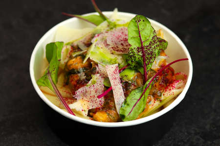 Pasta with mussels, cream sauce, parmesan and greens in a round paper takeaway food container on a...
