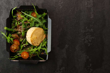 Savory souffle salmon and salad with arugula, tomatoes and green beans in black paper takeaway box...