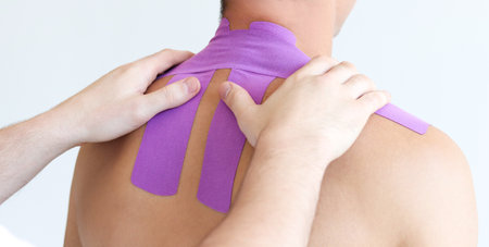 Kinesiology taping. Kinesiology tape on patient neck. Young male athlete on white background. Post traumatic rehabilitation, sports physical therapy, recovery concept.の写真素材