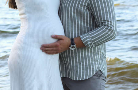 Pregnant woman and husband hugs belly against the background of the sea. Image of pregnant couple....