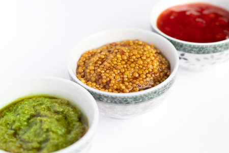 Sauce set - ketchup, pesto and mustard seeds in gravy bowls isolated on white background
