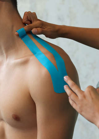 Close up of physiotherapist applying blue tape on patient's neckの写真素材
