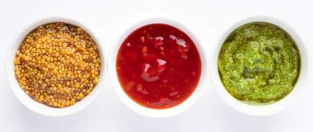 Sauce set - ketchup, pesto and mustard seeds in gravy bowls isolated on white backgroundの写真素材