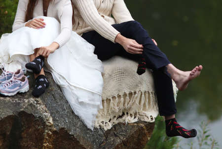 Close-up of the legs of a young couple sitting on a stone by the lakeの写真素材