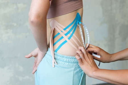Close up of physiotherapist doing kinesio tape on patient's back.