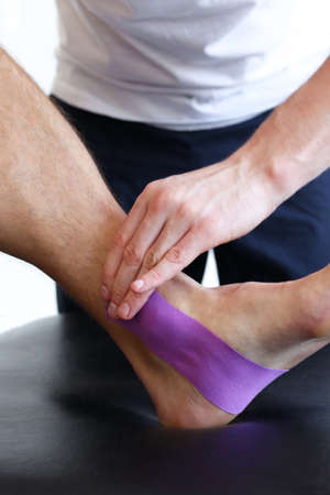 Kinesiology taping treatment with purple tape on male patient injured foot. Sports injury kinesio treatment.の写真素材