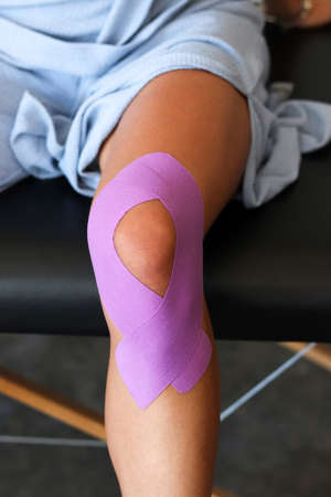 Physiotherapist applying kinesiology tape to patient knee. Therapist treating young female athlete. Kinesiology taping. Post traumatic rehabilitation, sport physical therapy.の写真素材