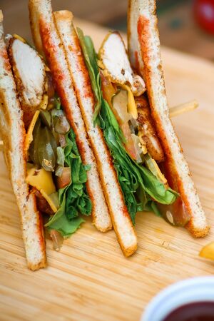 Sandwich with meat, salad, vegetables, lettuce, tomato, onion and mustard on a fresh sliced rye bread on wooden background. Close-up photo of a club sandwich.の写真素材