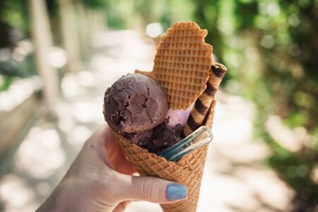 Girl holding melting ice cream waffles cone in hands on summer light nature background