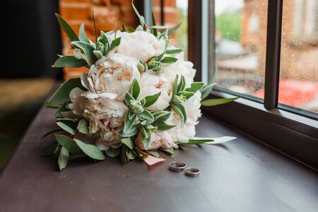 Bridal bouquet of peonies and rings on the windowsill. Close up.の写真素材