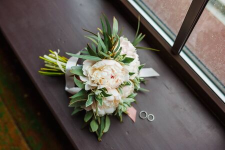 Bridal bouquet of peonies and rings on the windowsill. Close up.の写真素材