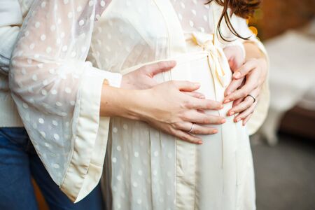 Image of a couple in expectation of baby. Future father is gently touching his pregnant wife belly. Elegant negligee for pregnant. Close up.の写真素材