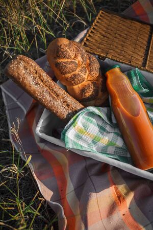 Picnic basket full with baguette and a bottle of juice on a homespun tablecloth, flat lay, selective focus. Vertical photoの写真素材