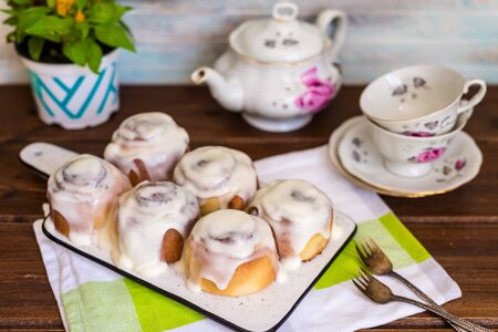 Cinnamon rolls or cinnabon, homemade sweet traditional dessert buns with white cream sauce on a wooden background with tea  pot and small tea cups , top viewの写真素材