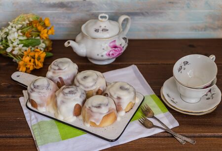 Cinnamon rolls or cinnabon, homemade sweet traditional dessert buns with white cream sauce on a wooden background with tea  pot and small tea cupsの写真素材