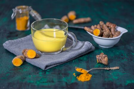 Turmeric Latte or golden milk with fresh turmeric roots on green background