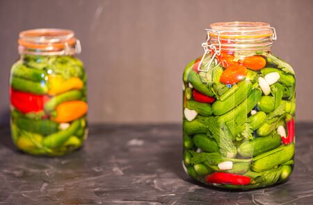 Preserves or pickled vegetables in glass jars. On the wooden black background.