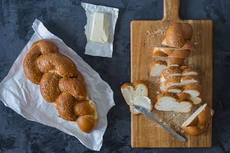 Jewish challah bread, sliced on black background, butter and knife, top view or flat lay