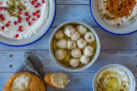 Popular middle eastern appetiser labneh or labaneh, soft white goat milk cheese with bread,4 different kinds of serving, hyssop, red paprika, pomegranate, labneh balls, over rustic table, top viewの写真素材