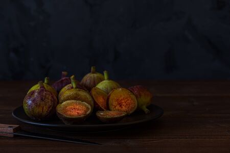 Fresh figs. Dark photo of a figs in black plate on wooden rustic surface, front view. Copy space. Food Photographyの写真素材