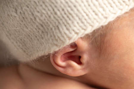 Close up of a new born baby ear with white knitted hat.